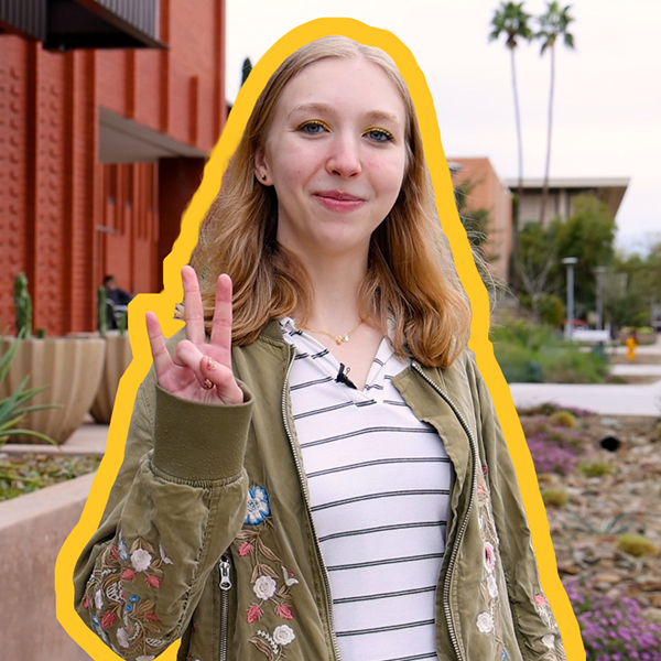 A woman with a striped shirt and green jacket show the pitchfork with her fingers. 