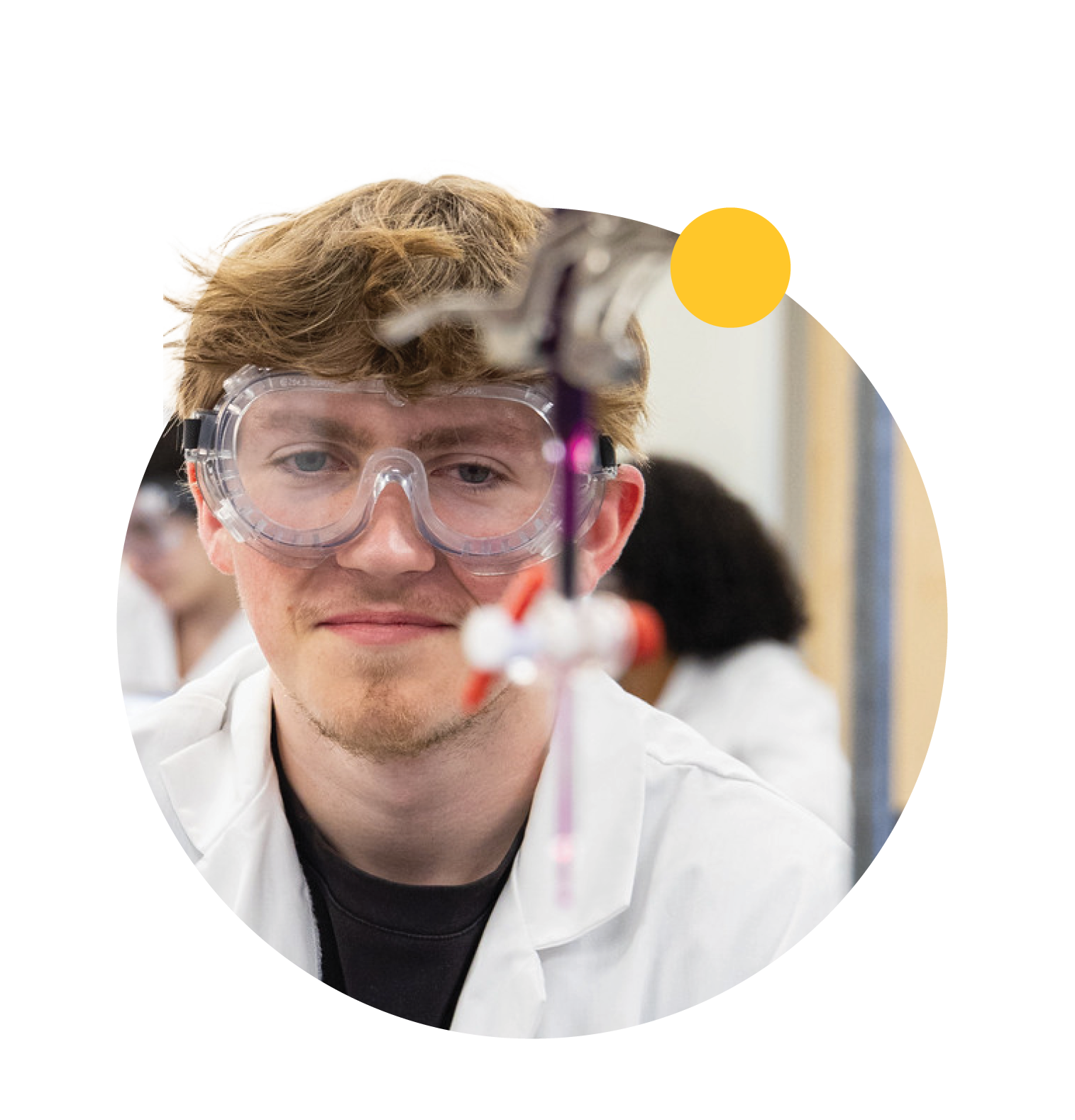 A student wears goggles and looks at blurred chemistry equipment in the foreground.