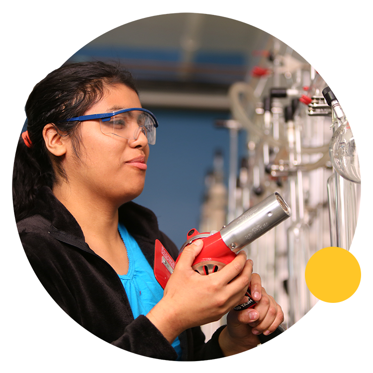 Student wearing safety glasses and pointing a heat gun at glass flask