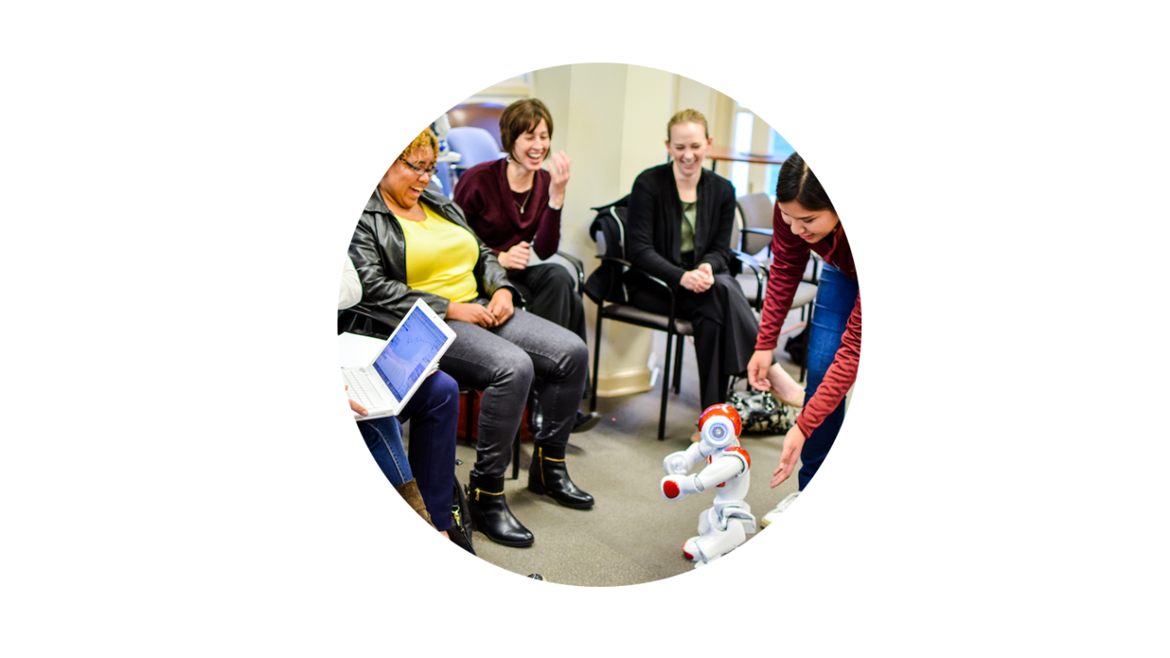 Women gather and interact with a robot.