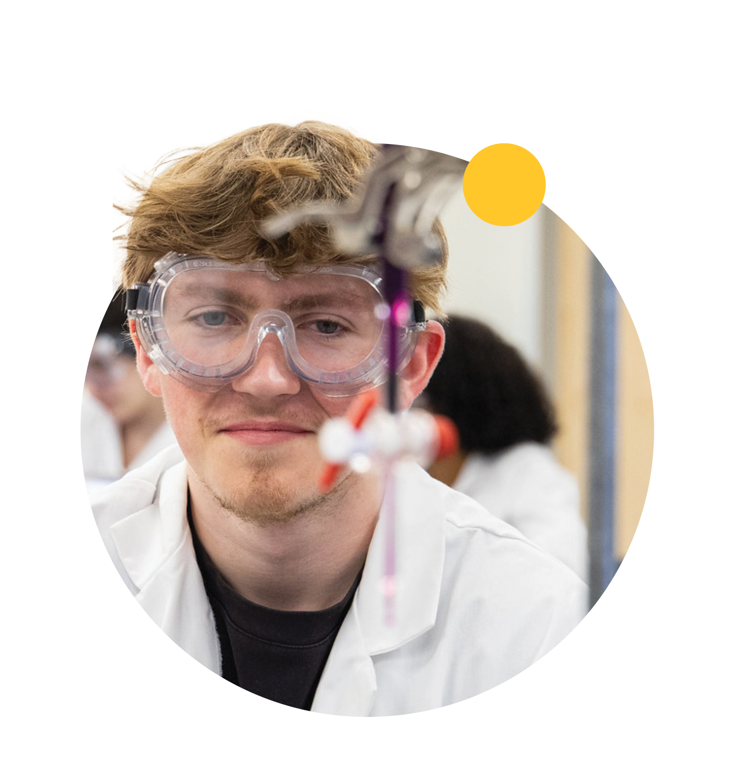 A student wears goggles and looks at blurred chemistry equipment in the foreground.
