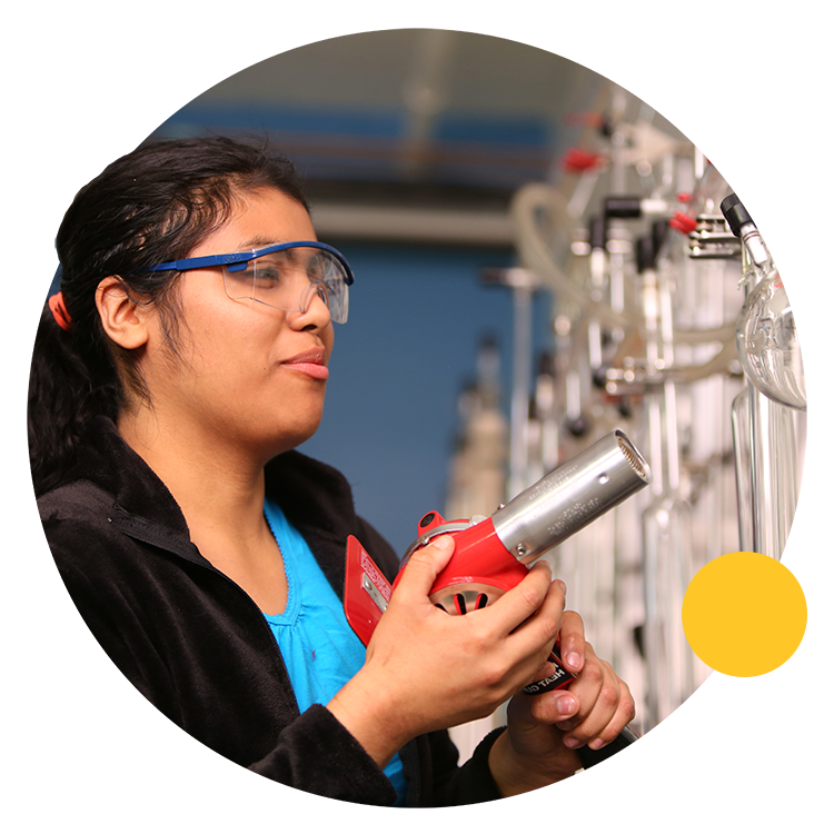 Student wearing safety glasses and pointing a heat gun at glass flask