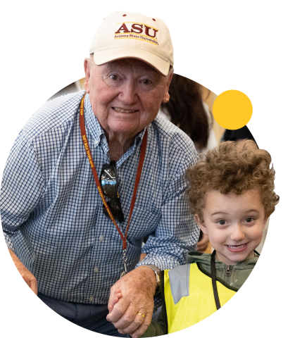 A young child and an elderly man hold hands and smile.